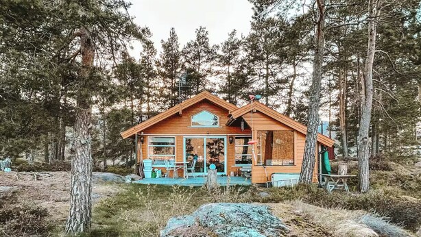 Une cabane en bois dotée d’un porche, entourée d’arbres.