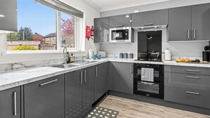 A modern kitchen with grey cabinets, a stainless steel refrigerator, a microwave, and a stove. - 3 Bedroom Home • Garden View • Parking • Fast WIFI (Blackburn with Darwen)
