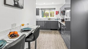 A modern kitchen with grey cabinets, a marble countertop, and a dining area with a table set for two. - 3 Bedroom Home • Garden View • Parking • Fast WIFI (Blackburn with Darwen)