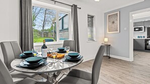 A modern dining area with a round table, grey chairs, and a view of the outdoors. - 3 Bedroom Home • Garden View • Parking • Fast WIFI (Blackburn with Darwen)