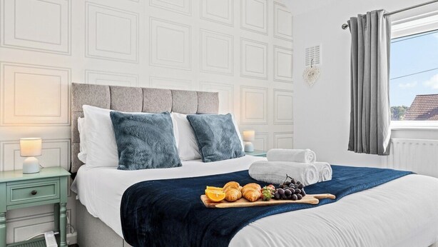 A neatly made bed with pillows, a bedside table with a lamp, and a tray of food. - 3 Bedroom Home • Garden View • Parking • Fast WIFI (Blackburn with Darwen)