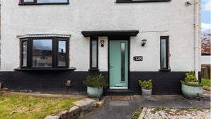 A two-story house with a green door, numbered 128, and a small garden with potted plants. - 3 Bedroom Home • Garden View • Parking • Fast WIFI (Blackburn with Darwen)