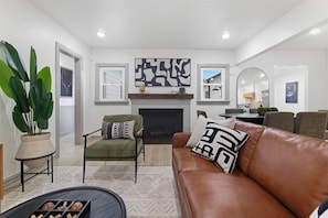 A living room with a fireplace, a green armchair, a brown leather sofa, and a large potted plant.