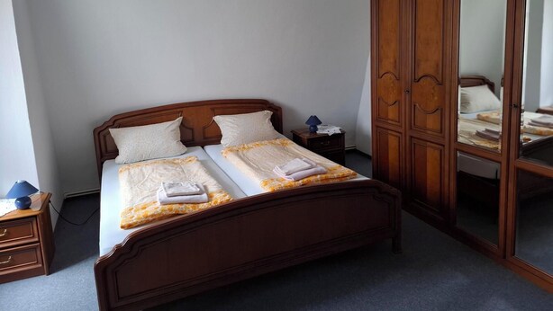 A bedroom with a wooden bed, a nightstand, a wardrobe, and a hanging lamp. - Weißes Roß (Crossen an der Elster)
