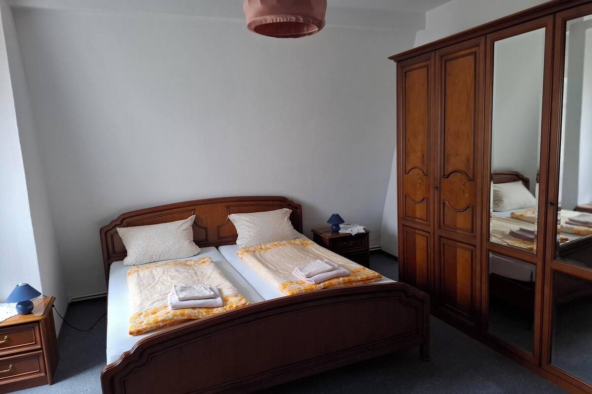 Une chambre à coucher avec un lit en bois, une table de chevet, une armoire et une lampe suspendue.