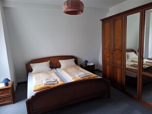 A bedroom with a wooden bed, a nightstand, a wardrobe, and a hanging lamp.
