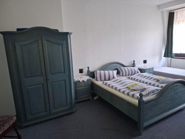 A bedroom with a bed, a wardrobe, a nightstand, and a window.
