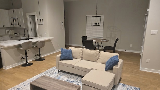 En moderne stue med sofa, skammel, sofabord og et spiseområde med bord og stole.