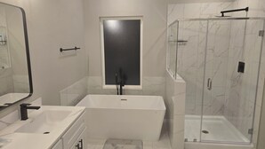 Et moderne badeværelse med badekar, bruseniche og et stort spejl.