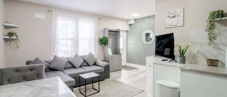 A modern living room with a sofa, a dining table, a TV, and a kitchen area.