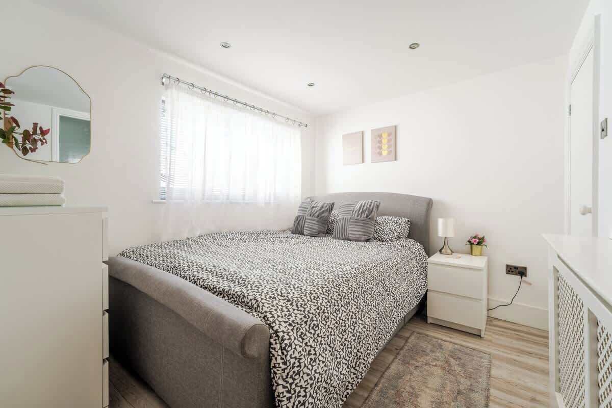 Un dormitorio con cama, mesita de noche, lámpara y espejo.