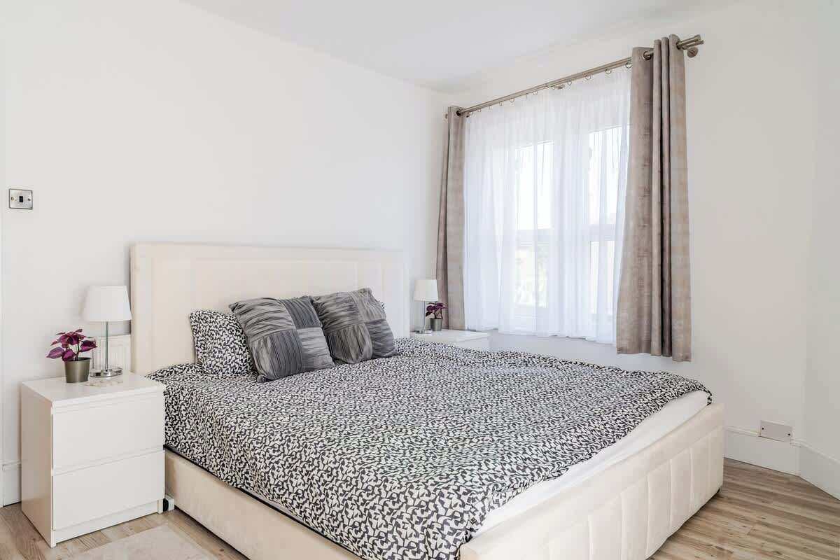 Une chambre à coucher avec un lit, une table de chevet, une fenêtre avec des rideaux et une prise électrique au mur.
