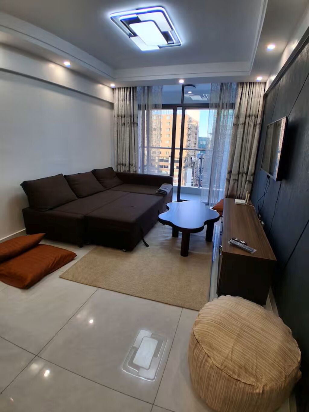 Uma sala de estar moderna com um sofá seccional, uma mesa pequena, um banco e uma TV fixada na parede.