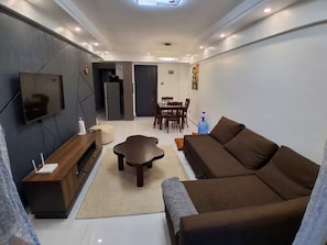 A modern living room with a sofa, TV, wooden entertainment unit, and a dining area with chairs and a table. - Chic 2BR with Gym & Skyline views - Westlands (Nairobi)