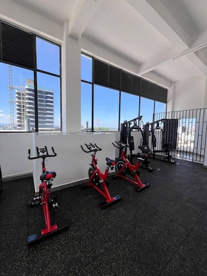 A gym with stationary bikes, exercise equipment, and large windows with a view of buildings. - Chic 2BR with Gym & Skyline views - Westlands (Nairobi)