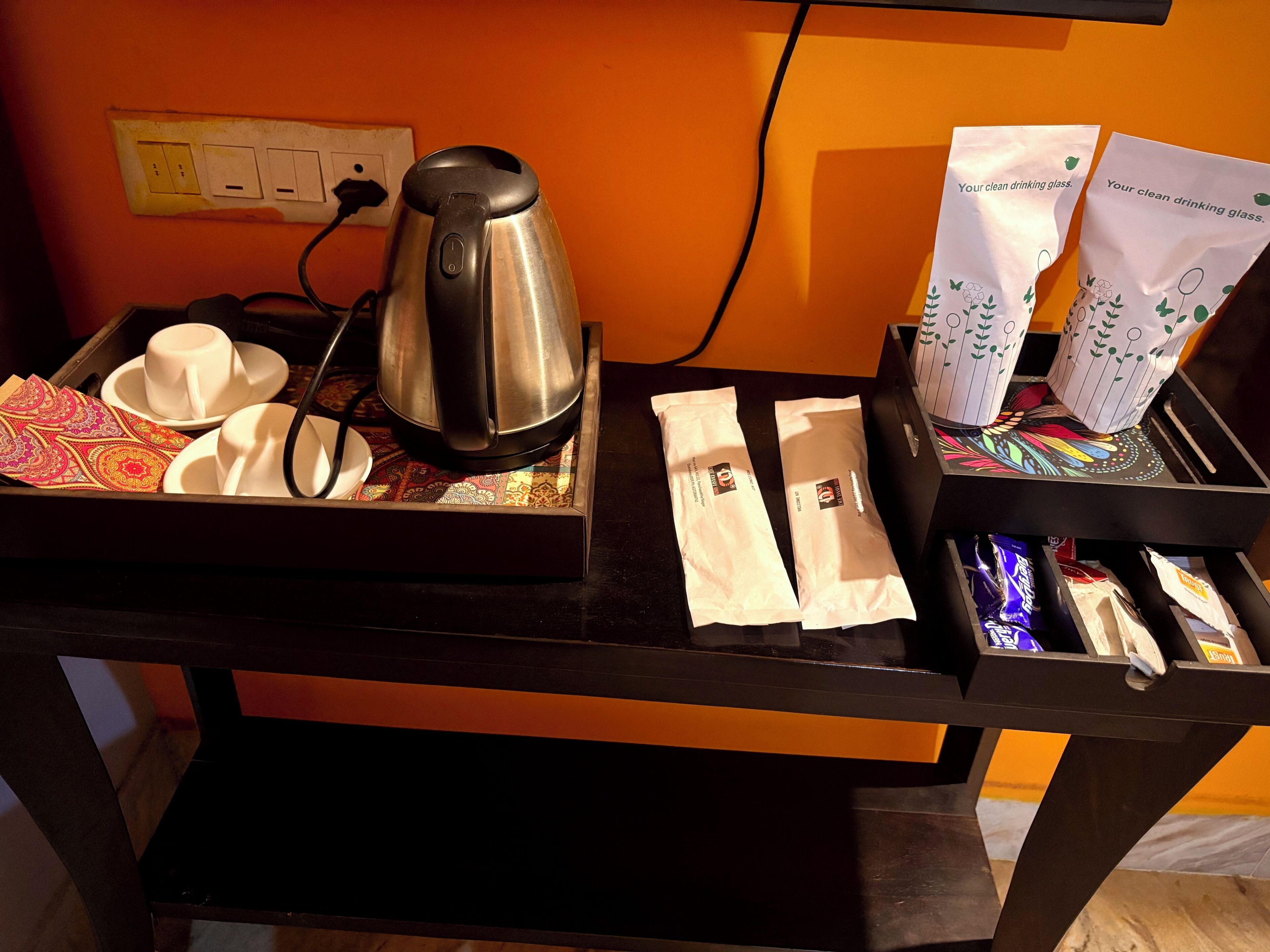 A table with a kettle, cups, saucers, a tray with a patterned cloth, and bags labeled 'Your clean drinking glass.'