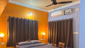 A bedroom with a bed, curtains, bedside lamps, an air conditioning unit, and a ceiling fan. - DEE DASH INN (Bhubaneshwar)