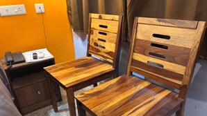 A wooden desk with a telephone and a small cabinet, a pair of wooden chairs with slatted backs, and a power outlet on the wall. - DEE DASH INN (Bhubaneshwar)