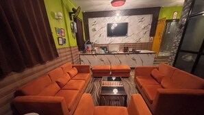 A living room with orange sofas, a coffee table, a TV, and a marble backsplash. - DEE DASH INN (Bhubaneshwar)