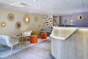 A modern reception area with a curved counter, seating with orange ottomans, and decorative wall mirrors.