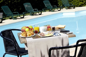 A poolside breakfast table with croissants, fruits, juice, and a sandwich.