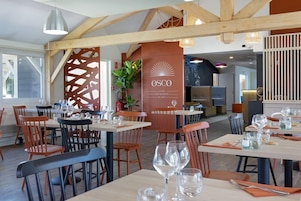 A restaurant interior with wooden beams, tables set with wine glasses, and a prominent OSCO sign.