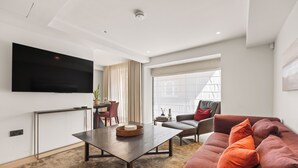 Una sala de estar moderna con televisor de pantalla plana, una zona de comedor con mesa y sillas, y un sofá con cojines.