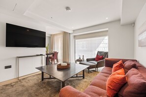 Ein modernes Wohnzimmer mit Flachbildfernseher, Essbereich mit Tisch und Stühlen sowie einer Couch mit Kissen.
