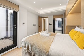A modern hotel room with a large bed, a sliding glass door to the balcony, and a separate door leading to the bathroom. - Mayfair Loft (London)