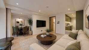 A modern living room with a sofa, coffee table, TV, dining area, and kitchen. - Mayfair Loft (London)