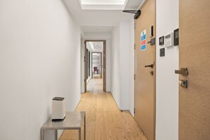 A hallway with a wooden floor, a white wall, and a door with a security system. - Mayfair Loft (London)