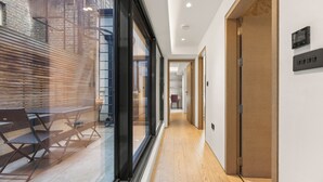 Un pasillo con piso de madera, pared de vidrio y un banco con sillas.