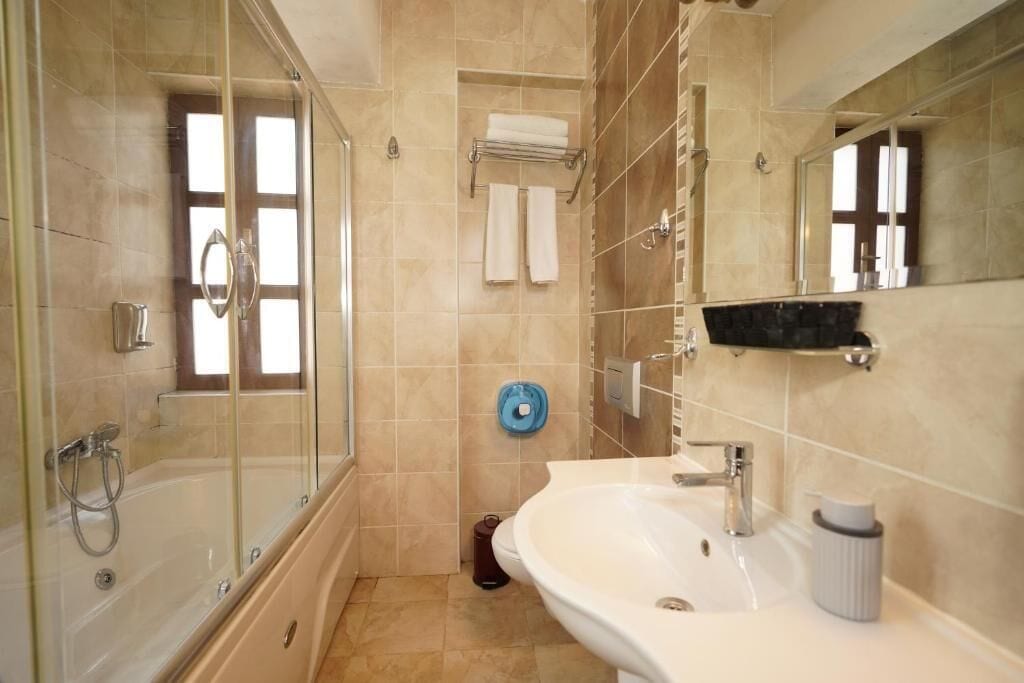 Un baño con ducha de vidrio, lavamanos blanco, espejo y toallero.