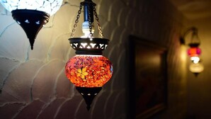 A hanging lantern with a patterned design, a wall with a textured surface, and a framed picture on the wall.