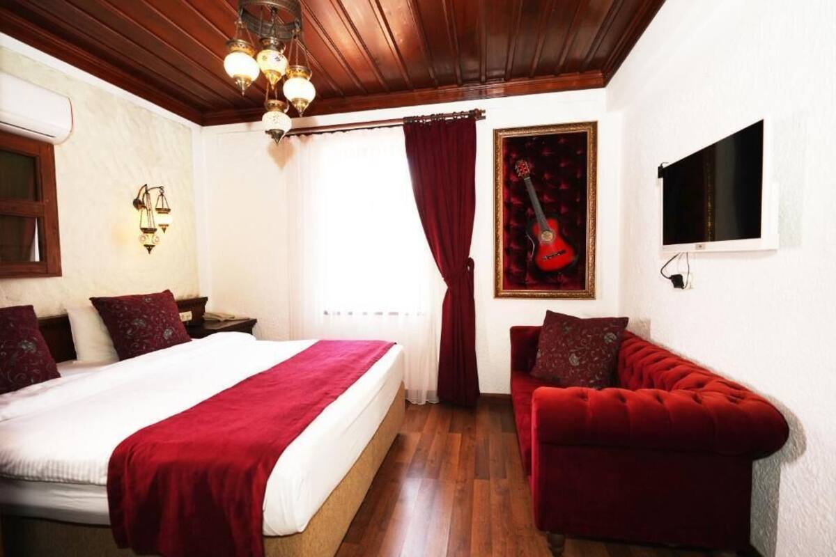 A bedroom with a bed, a red sofa, a guitar painting, and a TV.