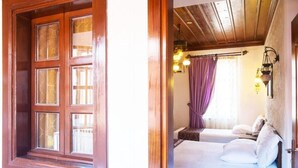 A room with a wooden door, a bed with white bedding, a nightstand, and a wall-mounted lamp.