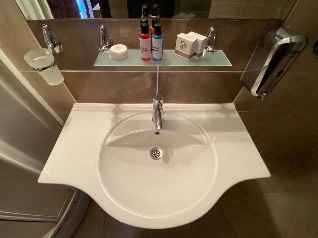 A bathroom with a white sink, a mirror, and a shelf with toiletries.