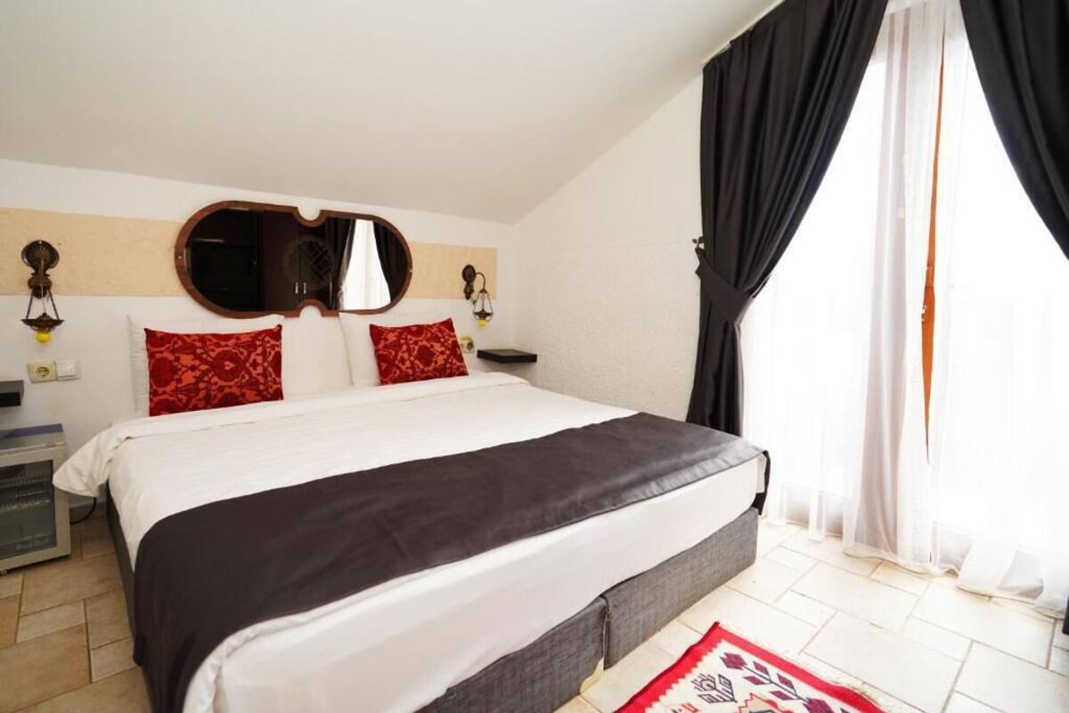 A bedroom with a bed, a mirror, a nightstand, and a window with curtains.