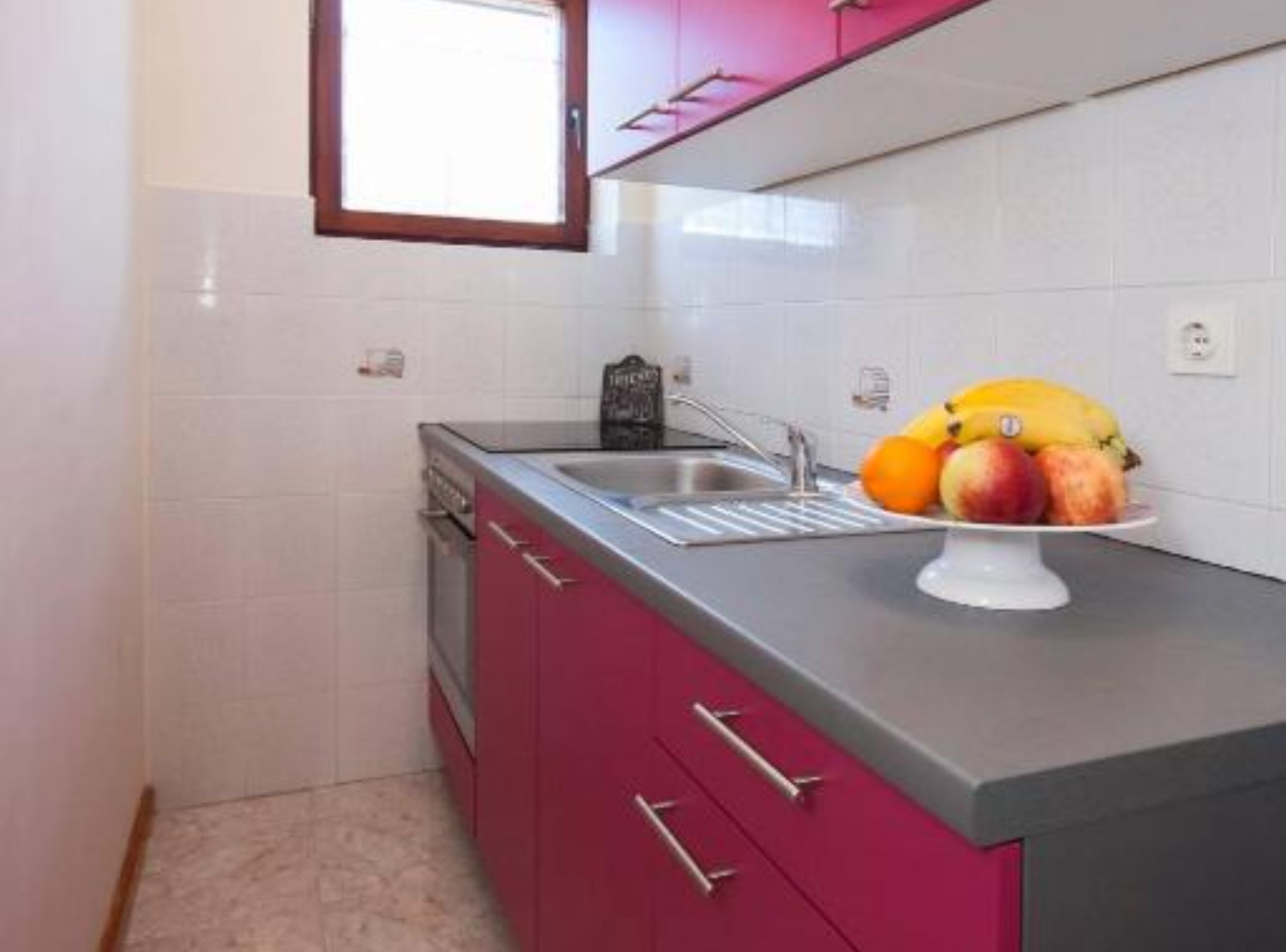 A kitchen with a sink, a dish rack, and a fruit bowl on the counter.