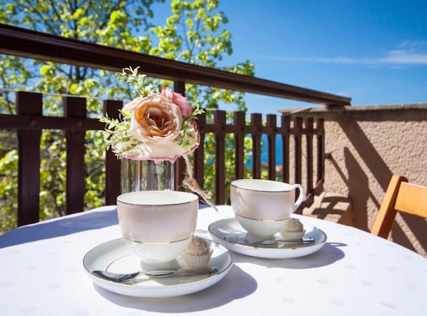 Una mesa con dos tazas y platillos blancos, un pequeño florero con una flor solitaria y un cupcake en una bandeja.