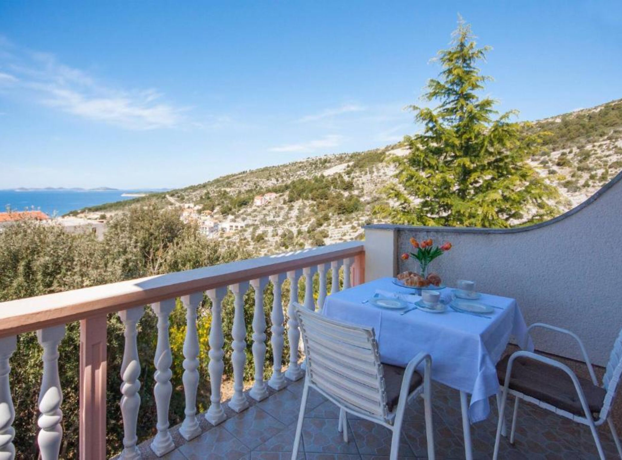 Un balcón con una mesa dispuesta para dos personas, con vista a un paisaje costero.