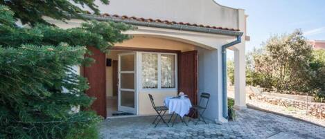 Un'area relax esterna coperta, con tavolo e sedie, un patio piastrellato e un edificio con tetto in tegole.