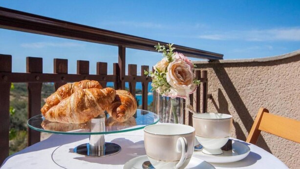 A table with croissants, a vase with flowers, and teacups on a balcony. - Guest House Stay & Smile Dolac Primošten (Primosten)