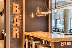 Una zona de bar con mostrador de madera, taburetes y luminarias colgantes.
