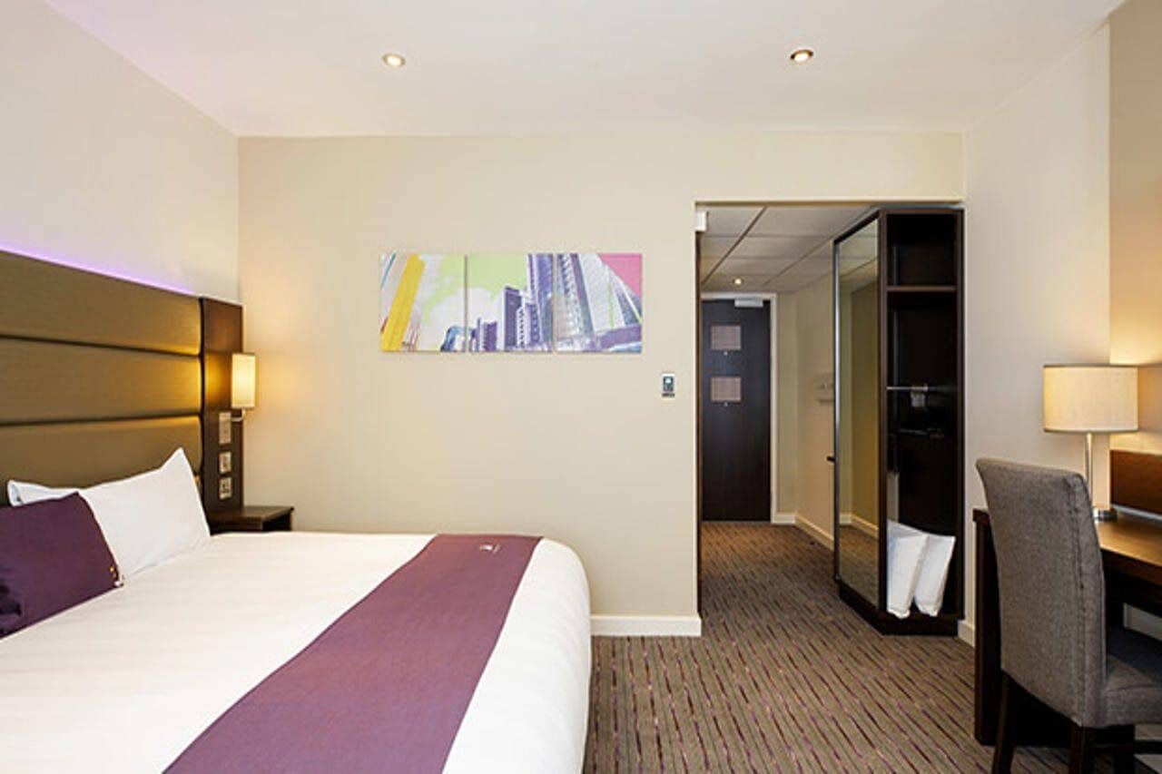 Quarto de hotel com uma cama, uma cadeira, uma mesa, um espelho e uma porta que dá para um banheiro.