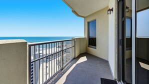 Ein Balkon mit Blick auf Strand und Meer, eine Glastür und ein kleines Fenster.