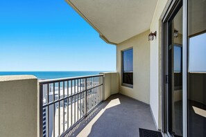 Ein Balkon mit Blick auf Strand und Meer, eine Glastür und ein kleines Fenster.