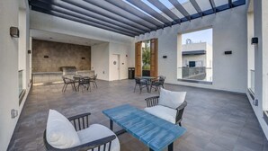 A covered outdoor patio with a grill, dining table, chairs, and a view of the city.