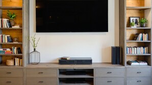 A modern living room with a large flat-screen TV mounted on the wall, surrounded by built-in shelving with books and decorative items.