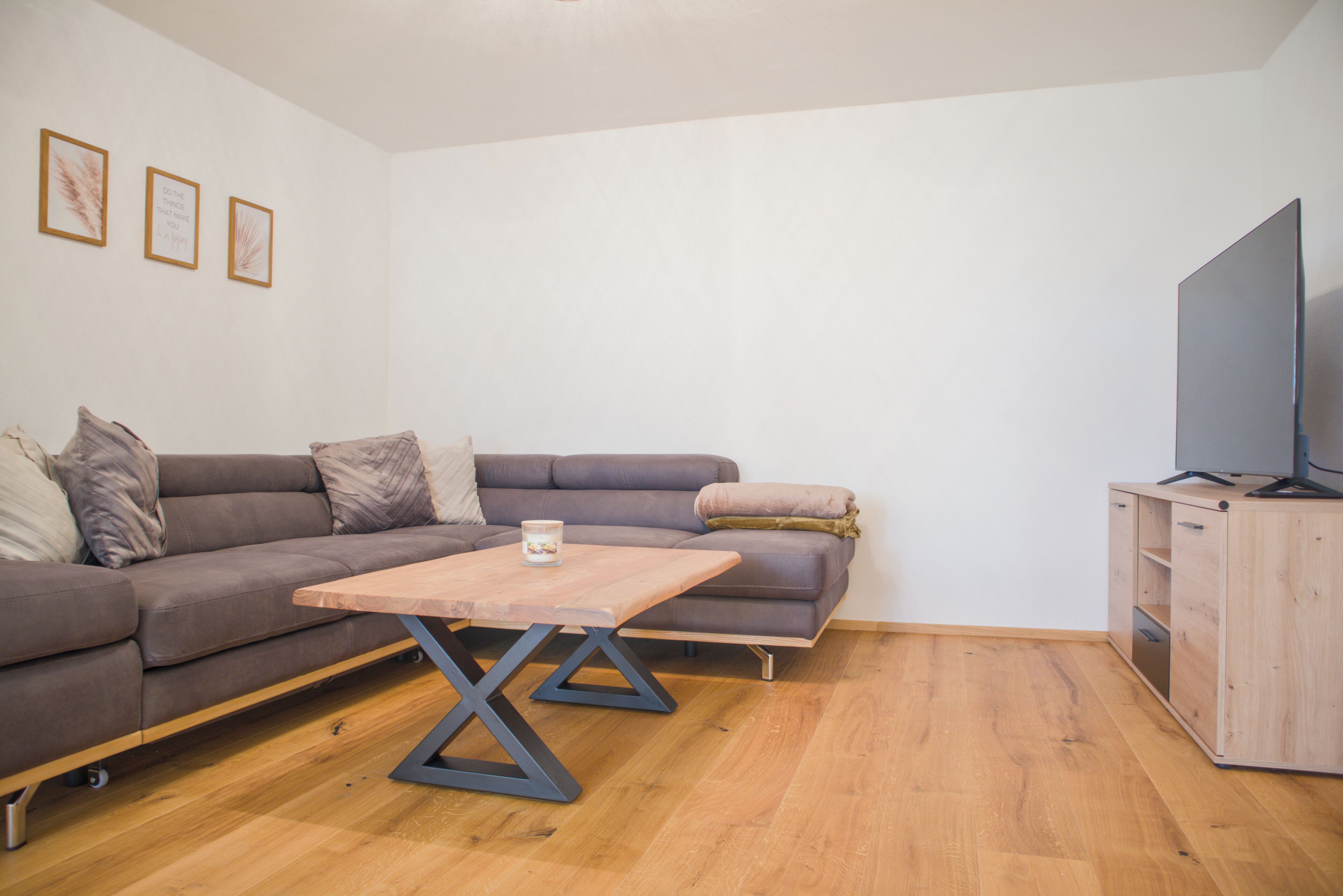 A modern living room with a sectional sofa, a wooden coffee table, a TV on a wooden cabinet, and framed artwork on the wall.